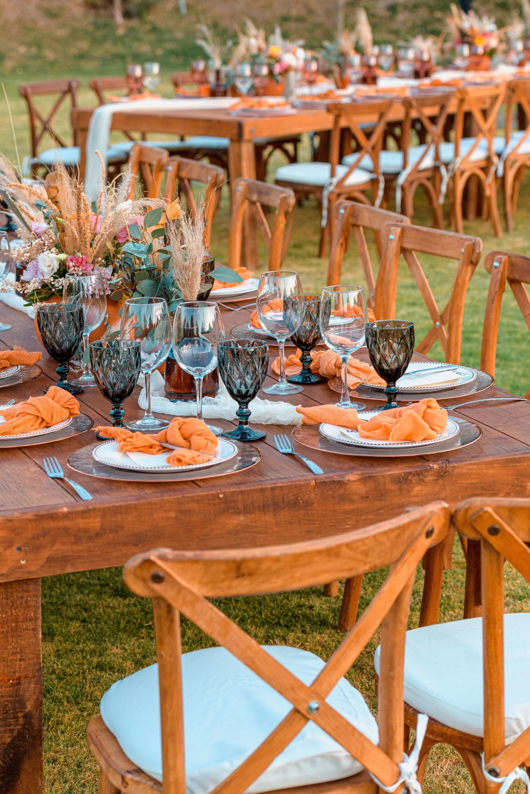jardines decorados para una boda de estilo boho con mesas y sillas de madera y copas de cristal de colores