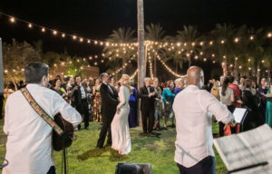 baile de novios en una boda al aire libre por la noche con los invitados de fondo y una guirnalda de luces