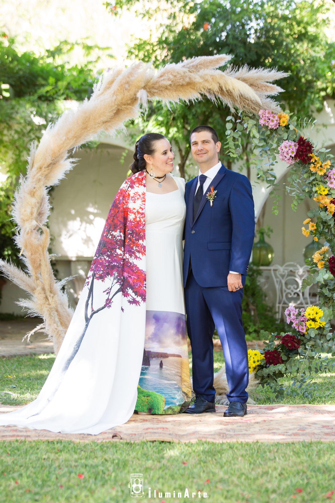 pareja de novios en su boda, con una decoración floral y un arco al fondo, la novia lleva un vestido de colores
