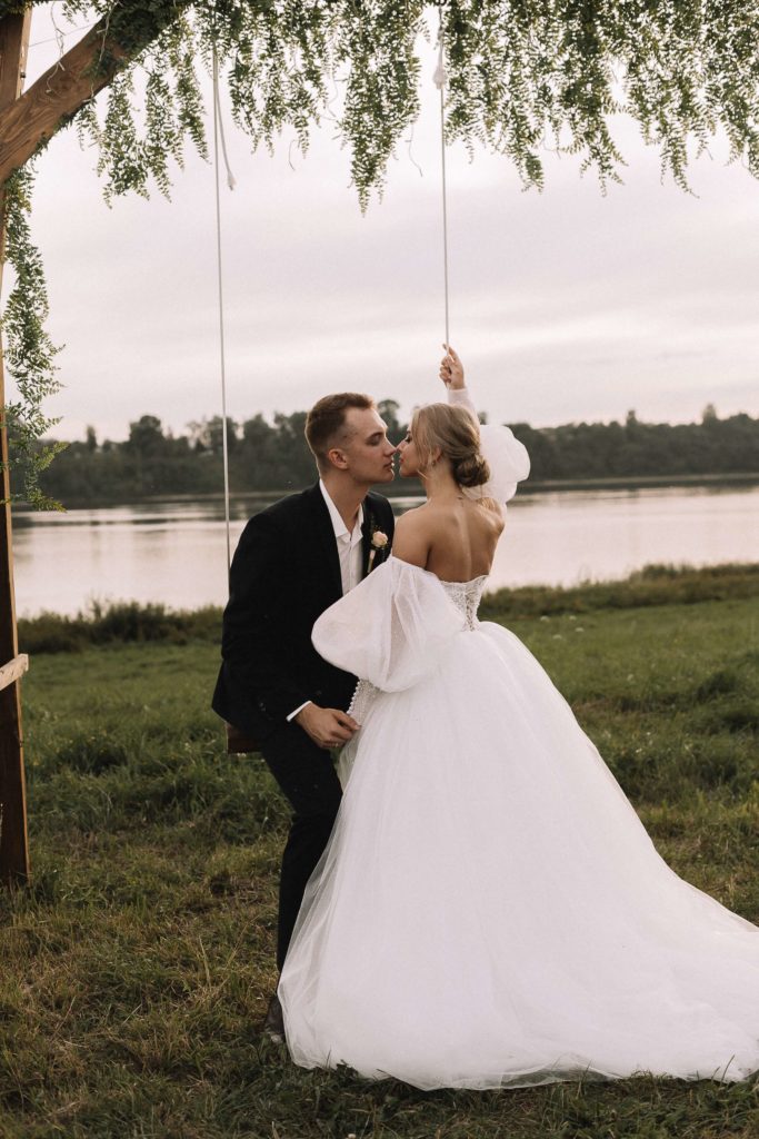 novios en un columpio con un lago al fondo, la novia lleva un vestido sin tirantes con guantes largos